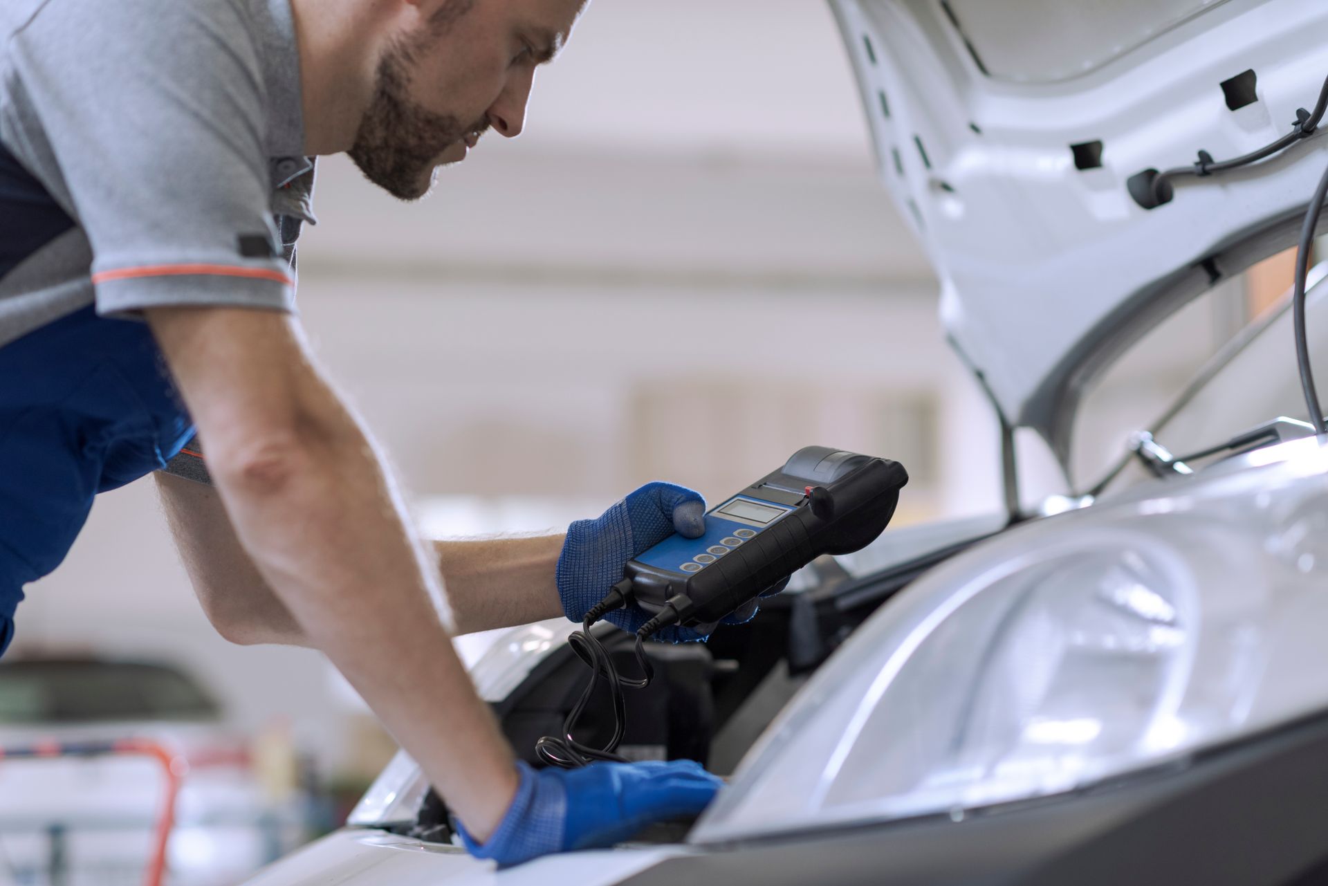 Mechanic using a diagnostic tool on a car with its hood open in a garage. Mechanic using a diagnostic tool on a car with its hood open in a garage.
