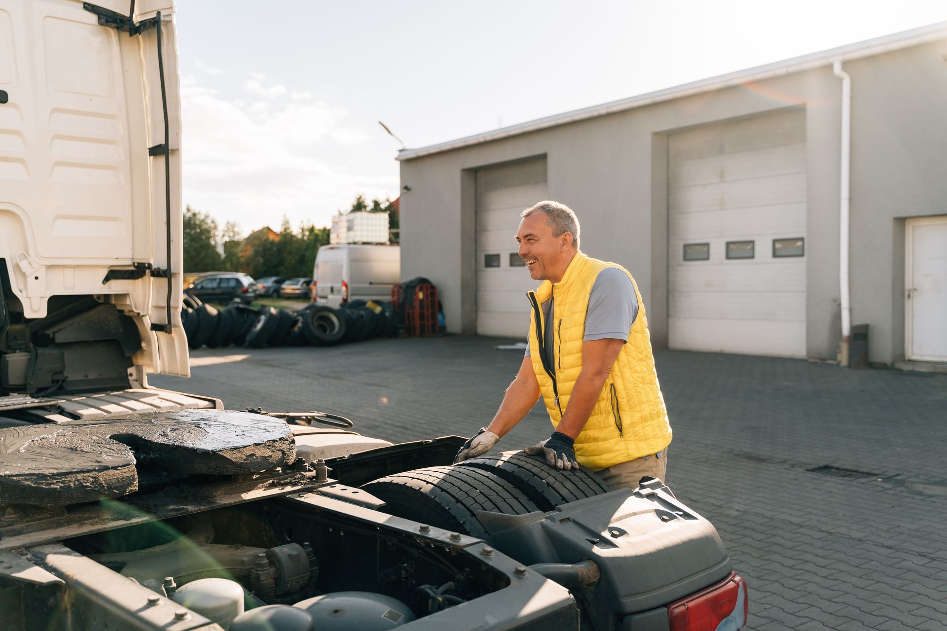 Truck driver in yellow vest, standing near a truck, smiling in front of a building.