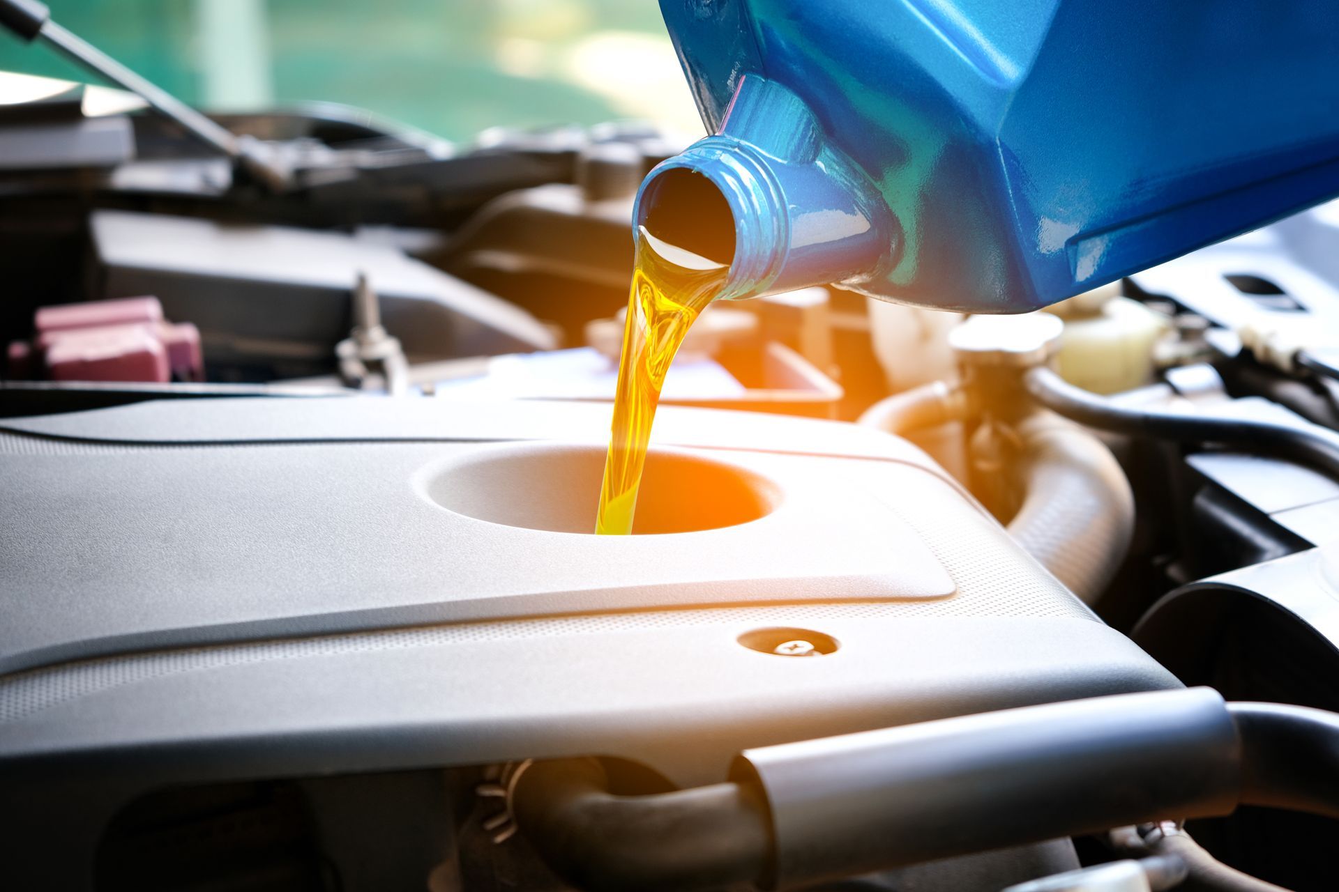 Pouring oil into a car engine; yellow liquid, blue container, close-up shot.