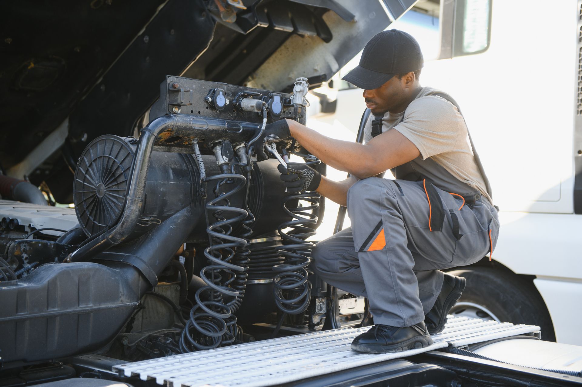 Mechanic working on the engine of a truck outdoors. He is kneeling in front of the open hood. Mechanic working on the engine of a truck outdoors. He is kneeling in front of the open hood.
