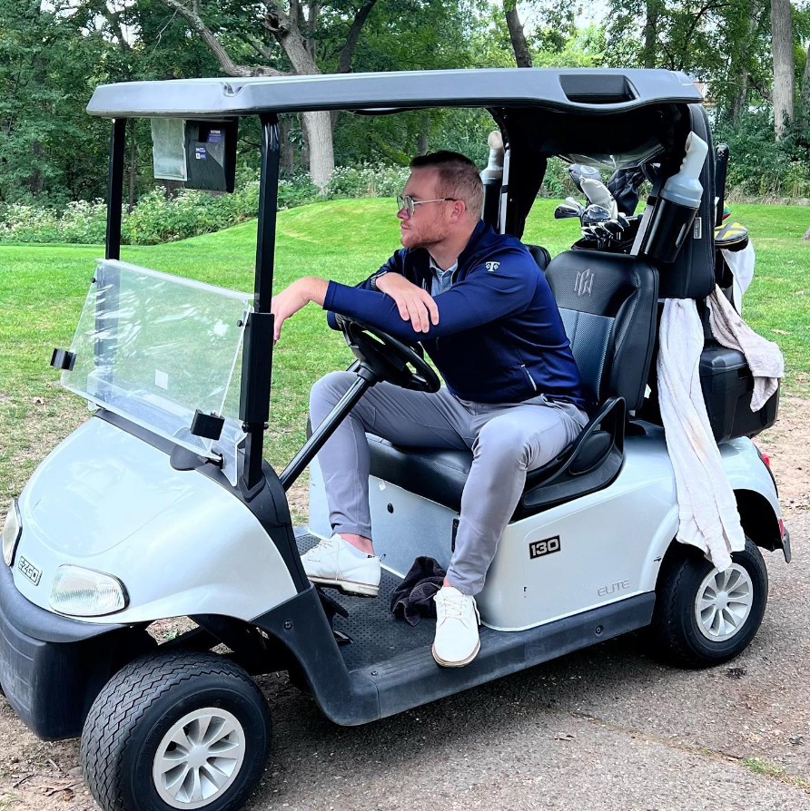 Andrew Knoll sitting on a golf cart at the golf course.