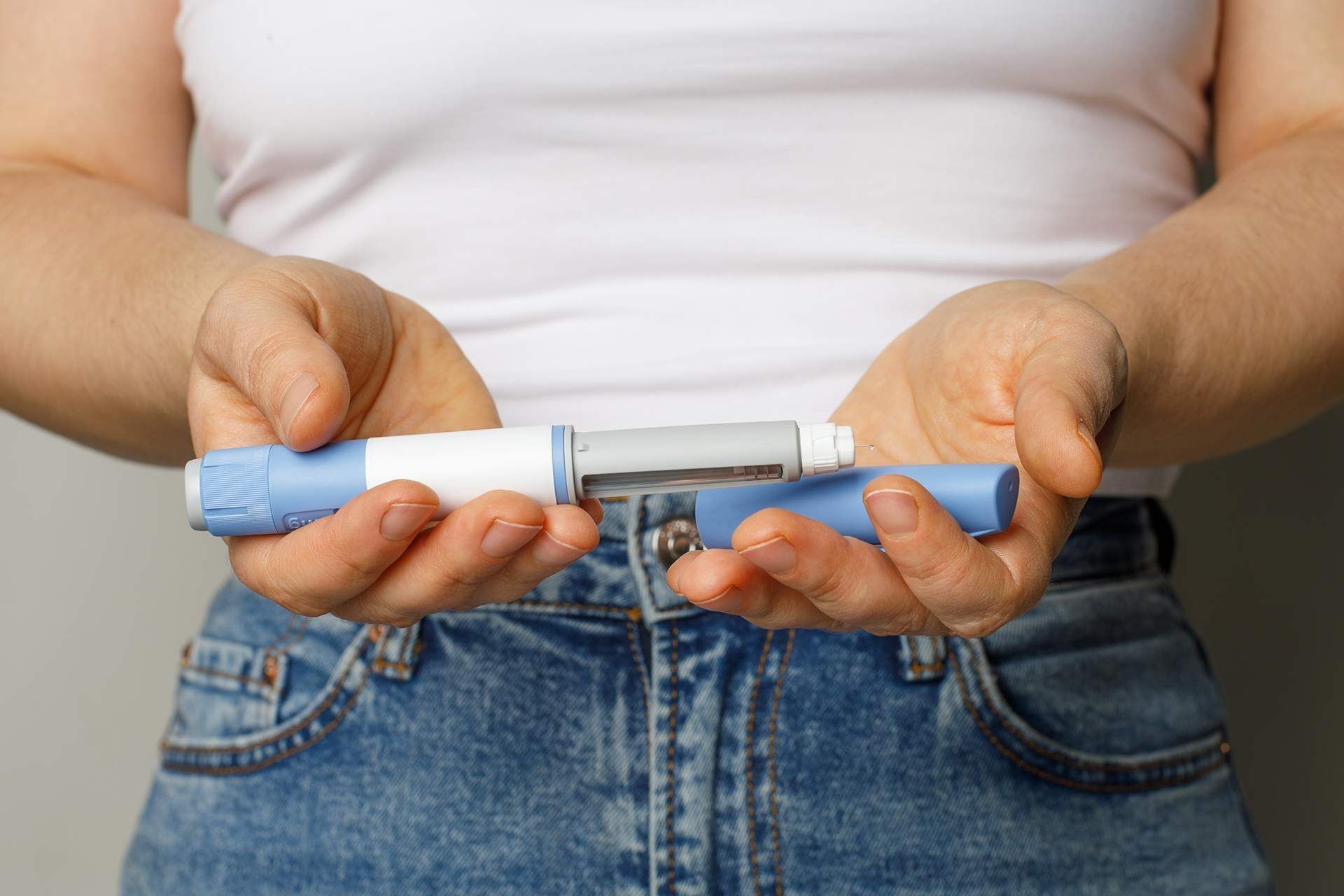 Person holding a blue and white insulin pen, wearing a white shirt and jeans.