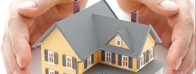 Manos ahuecando una casa modelo, lo que sugiere protección o seguro del hogar.