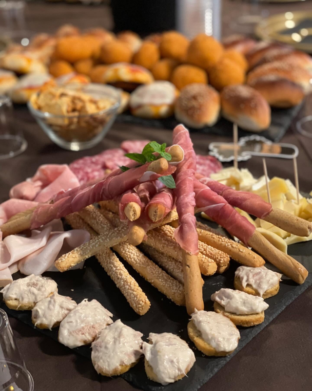 Tagliere di salumi con grissini avvolti nel prosciutto e altri antipasti.