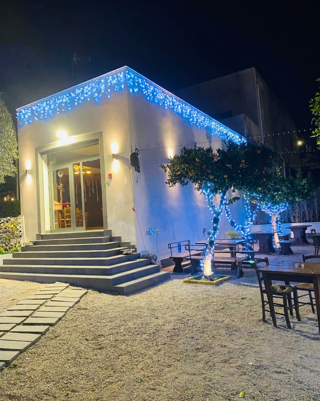 Esterno del ristorante di notte, edificio bianco con luci blu, posti a sedere all'aperto.