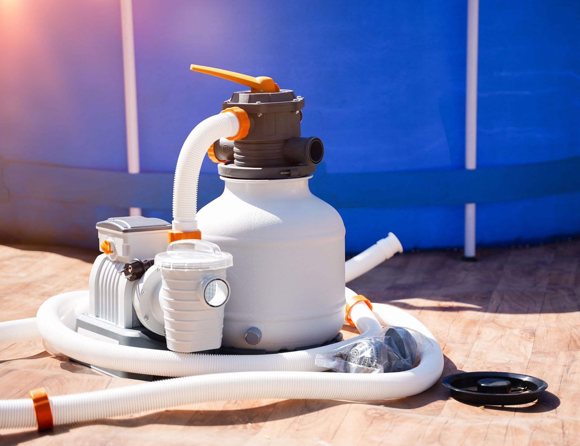 White pool filter and pump system on a wooden surface next to a blue above-ground pool.
