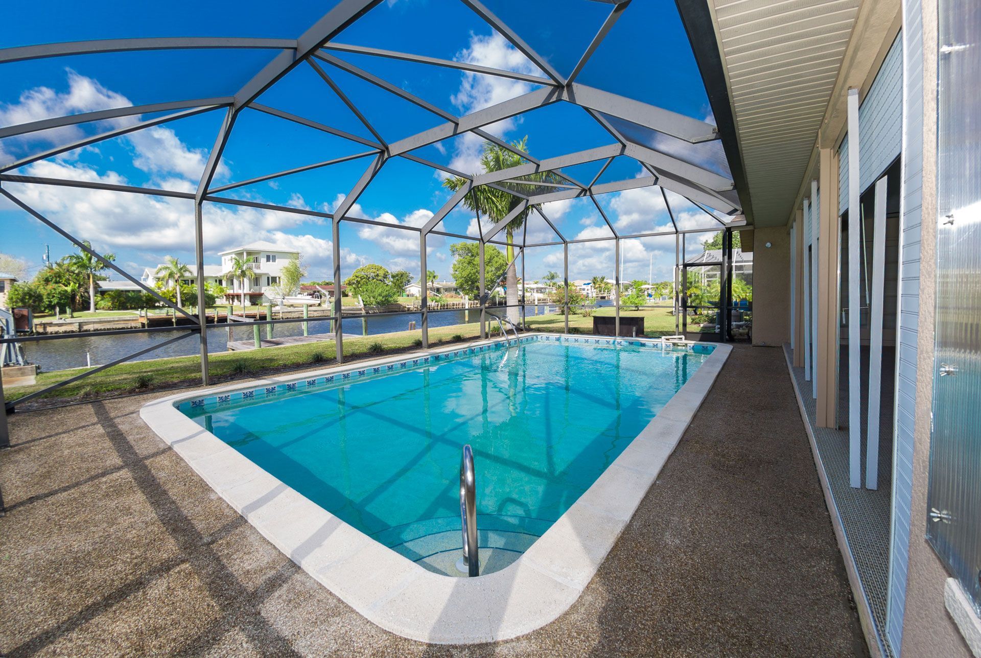Screened-in rectangular pool next to a home on a canal, with a blue sky visible through the screen.
