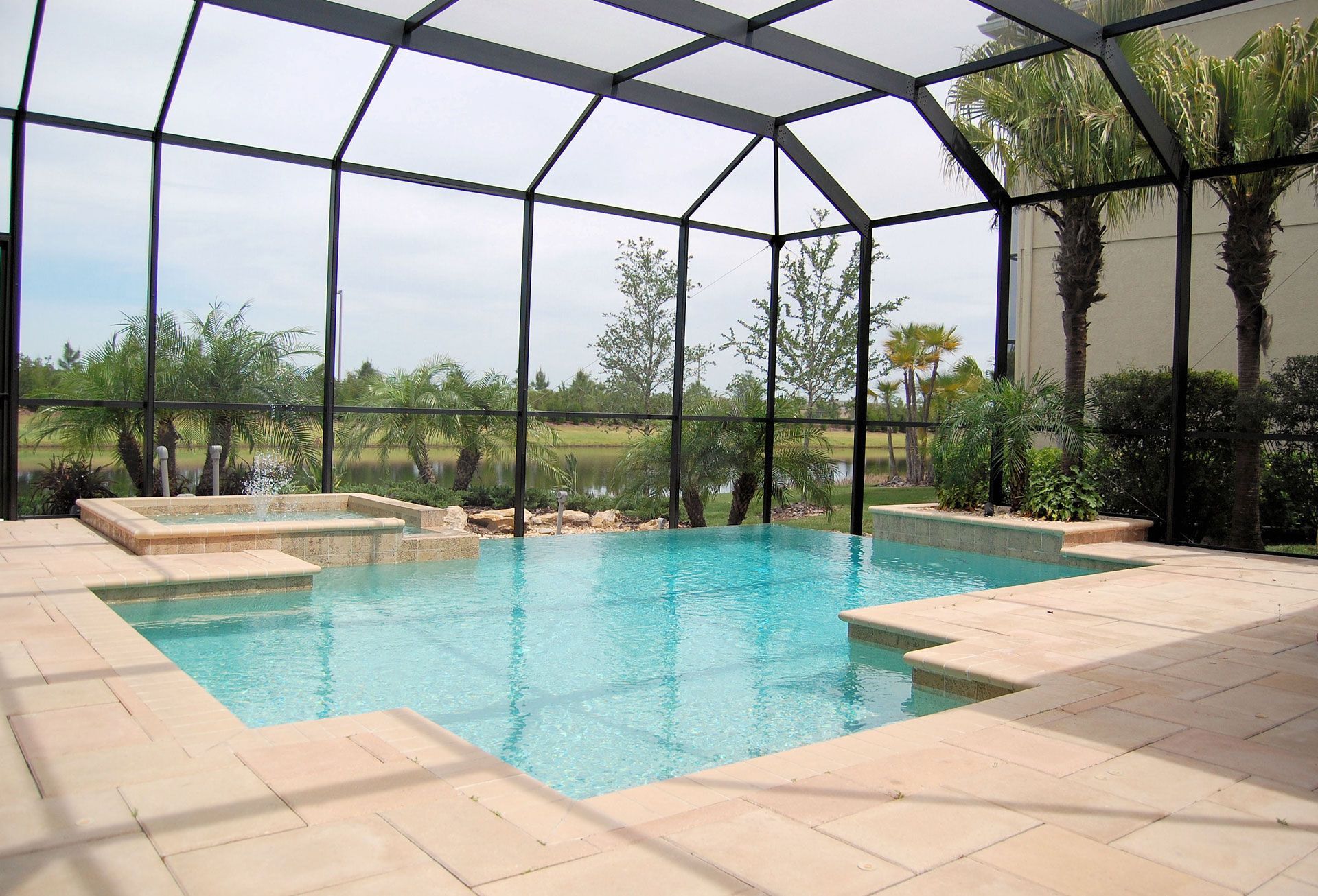 Pool enclosed in a screen with a surrounding patio and view of trees and a lake.