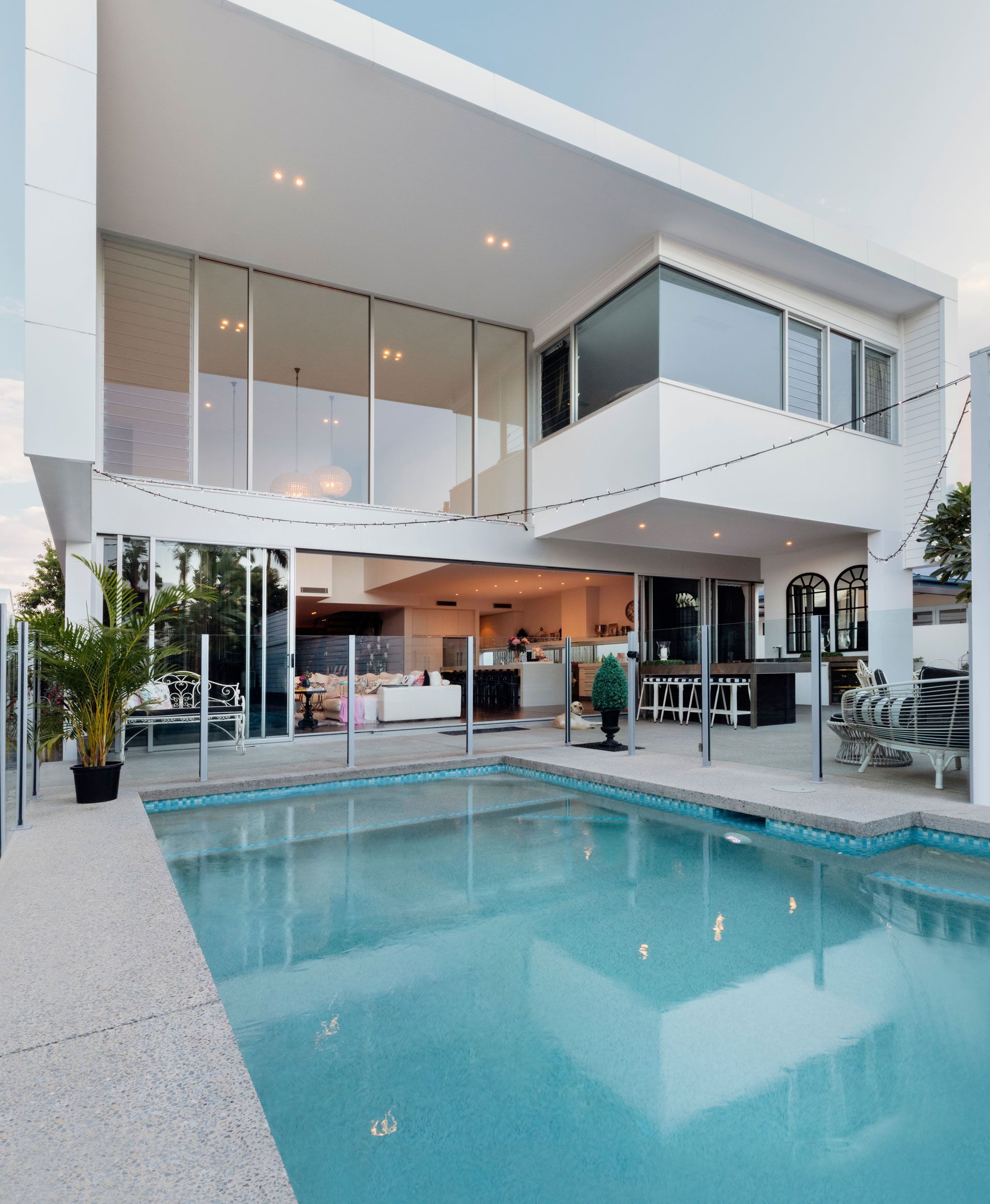 Modern white house with a pool. Large glass windows and outdoor seating.