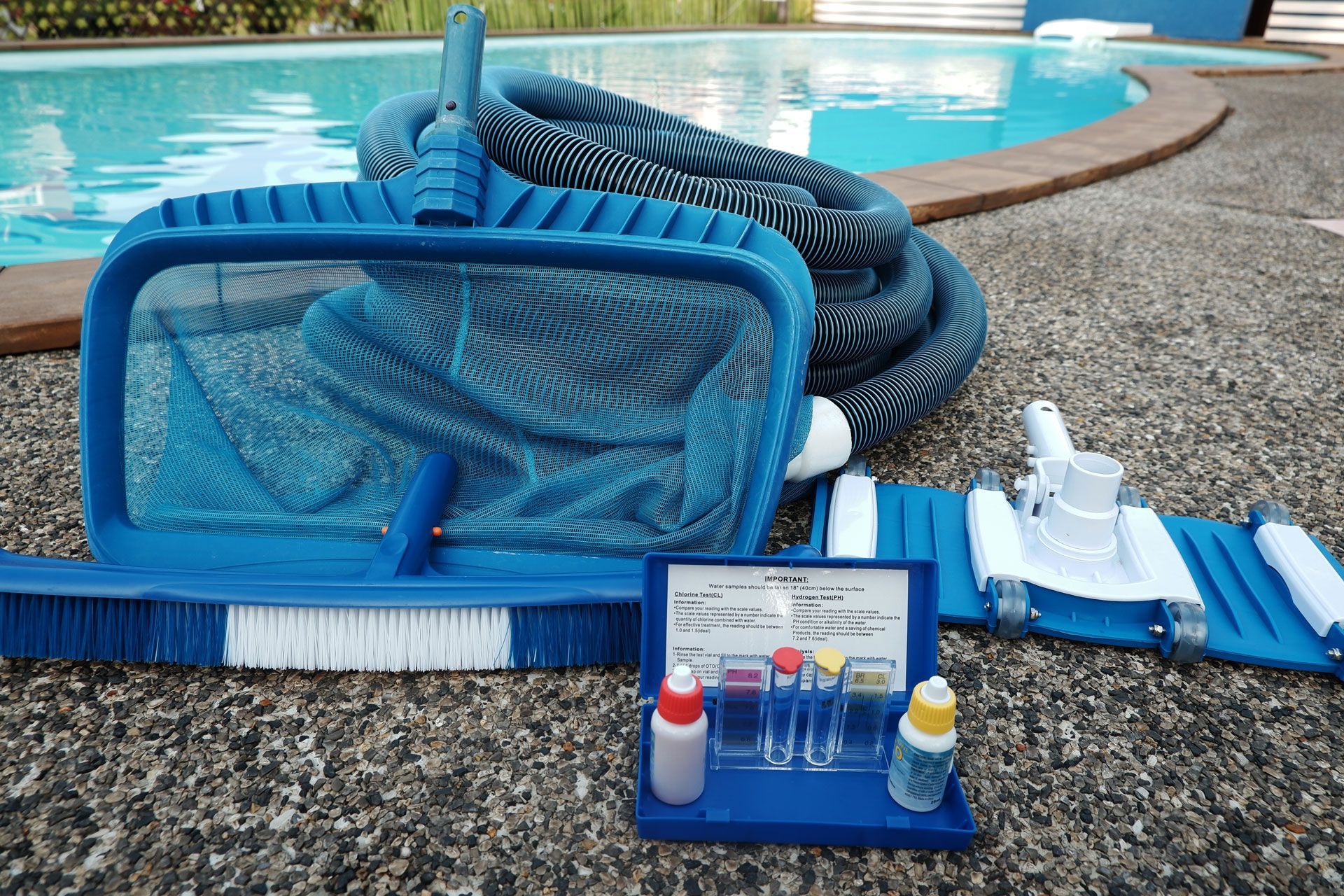 Blue pool cleaning tools and water testing kit on a pool deck.