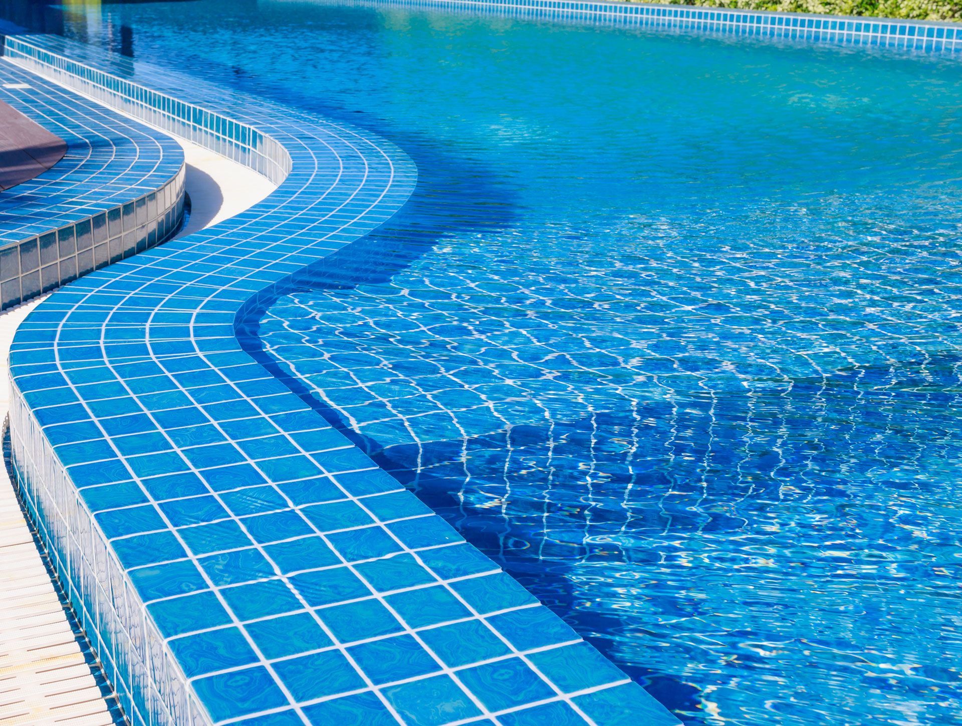 Blue tiled swimming pool with wavy edge, water shimmering in sunlight.