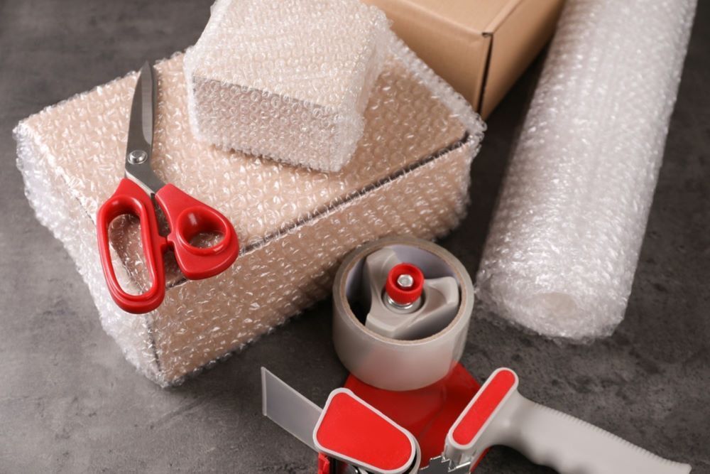 A Pair of Scissors Sitting on Top of a Box Next to a Tape Dispenser and Bubble Wrap — Bellarine Removals In Bacchus Marsh, VIC