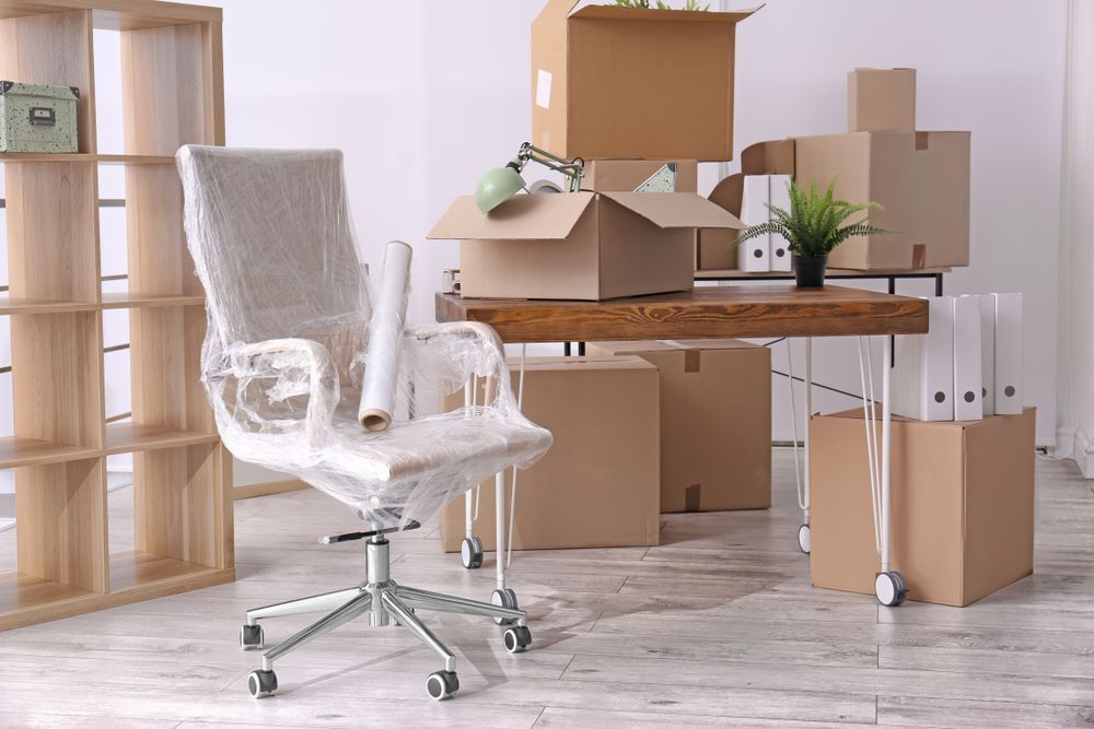 A Chair is Wrapped in Plastic in an Office Filled With Cardboard Boxes — Bellarine Removals In Bendigo, VIC