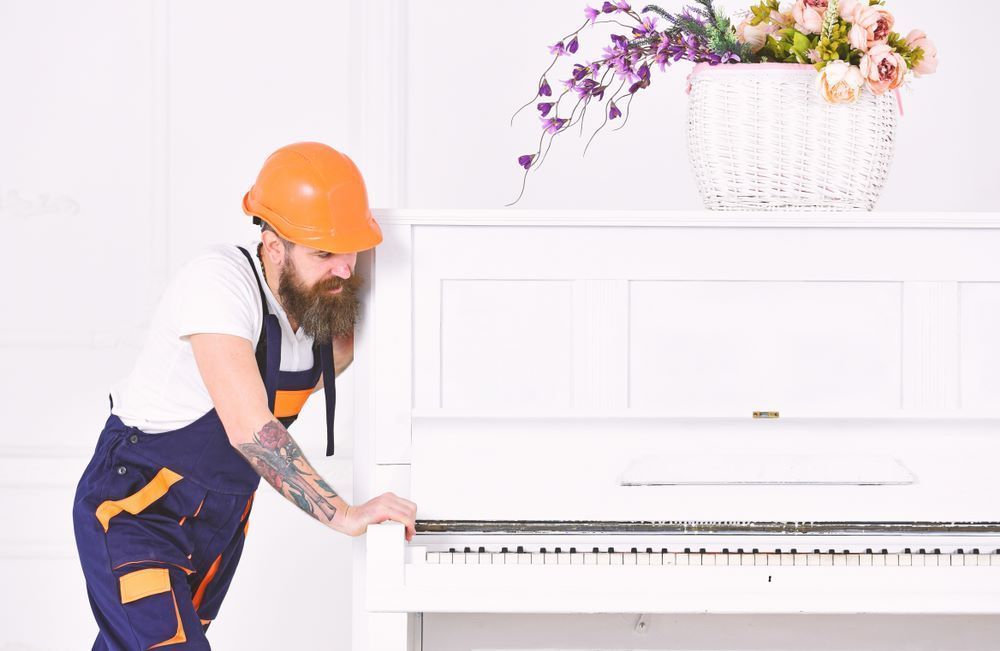 A Man Wearing a Hard Hat is Standing Next to a White Piano — Bellarine Removals In Bendigo, VIC