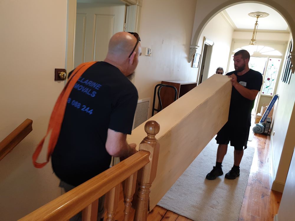 Two Men Are Carrying a Large Piece of Furniture Up a Staircase — Bellarine Removals In Bendigo, VIC