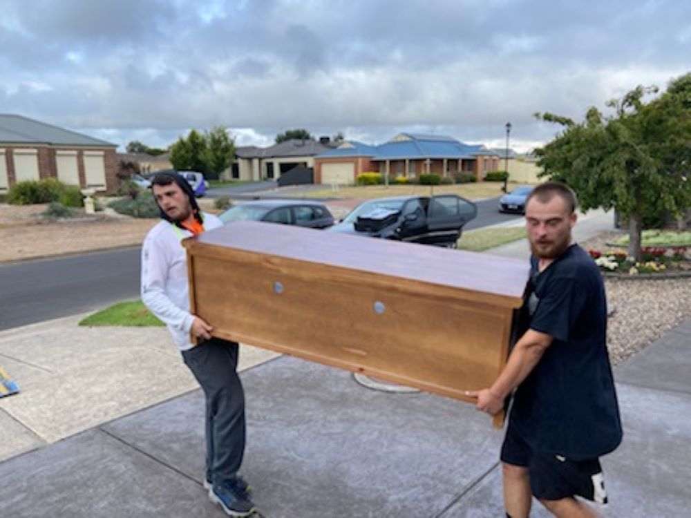 Two Men Are Carrying a Large Wooden Box on a Sidewalk — Bellarine Removals In Colac, VIC