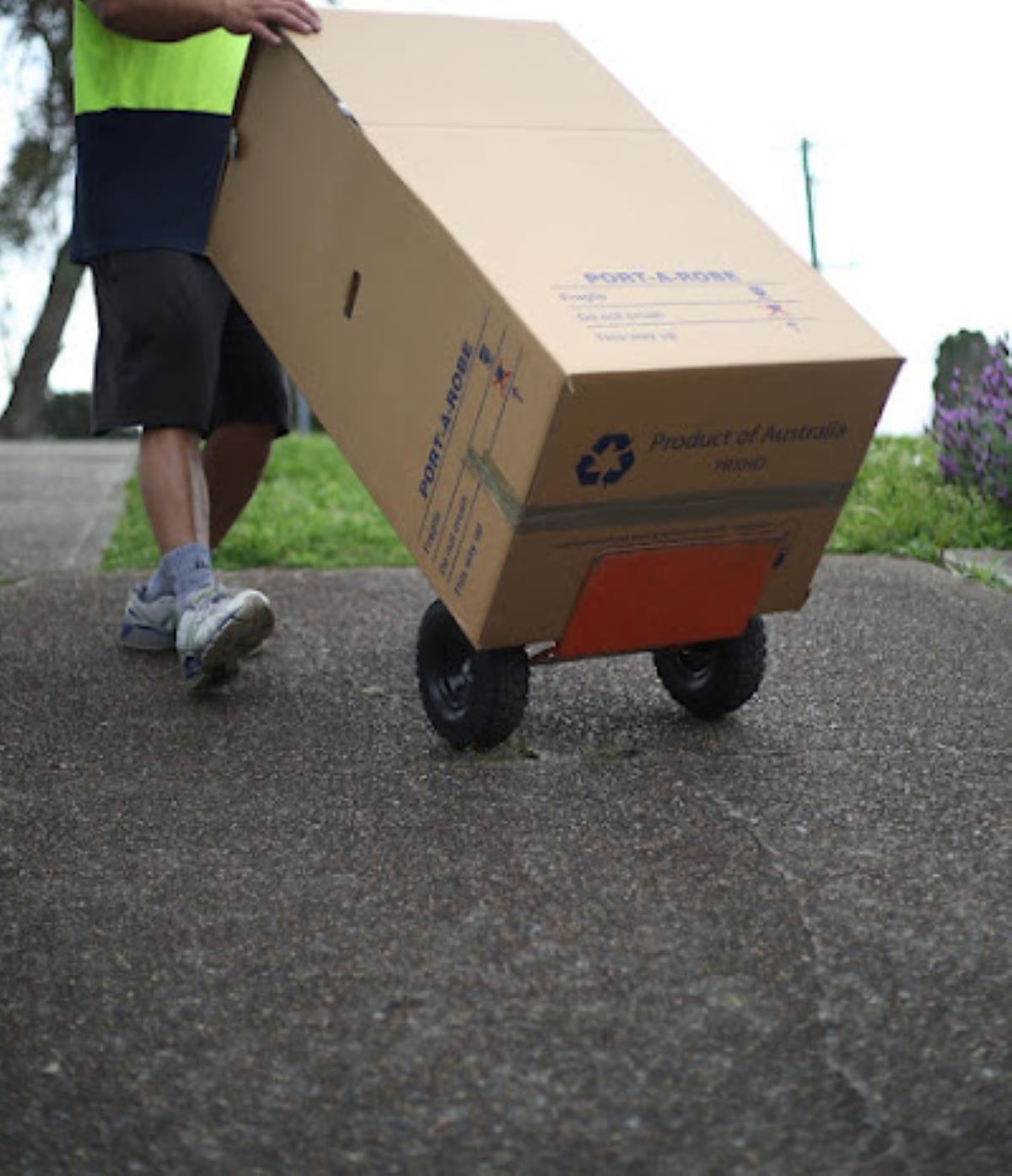 A Man is Pushing a Cardboard Box on Wheels — Bellarine Removals In Drysdale, VIC