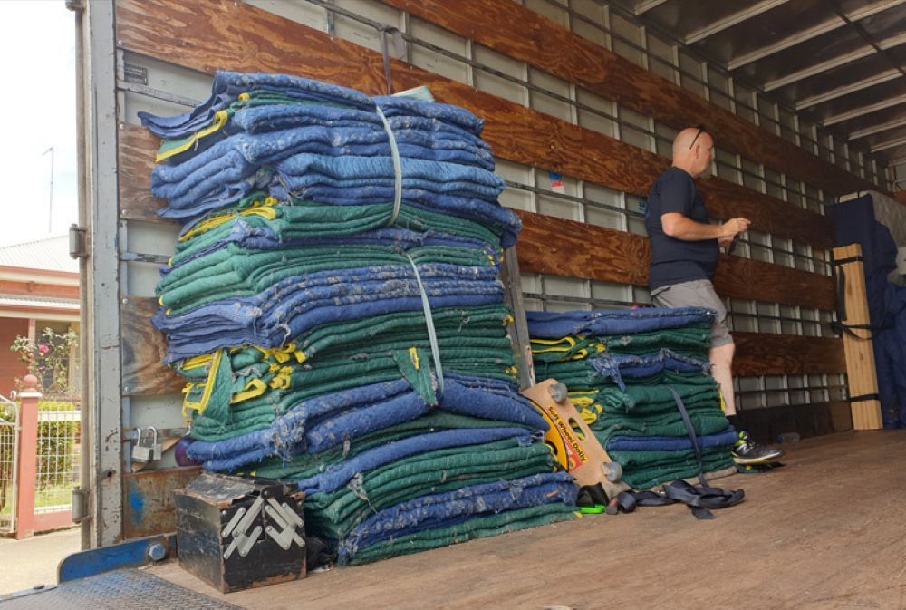 A Man is Standing Next to a Stack of Blankets in the Back of a Truck — Bellarine Removals In Melbourne, VIC