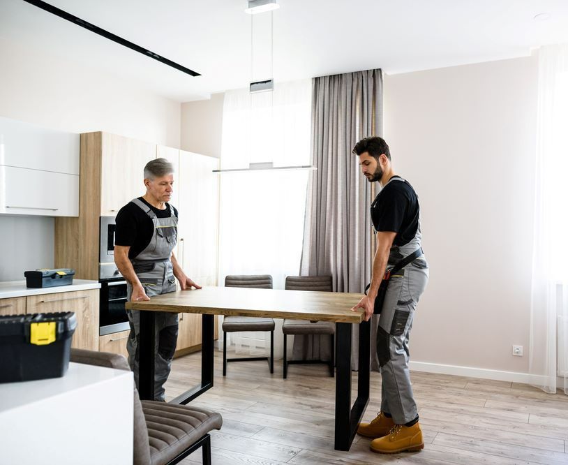 Two Men Are Standing Next to a Table in a Living Room — Bellarine Removals In Hoppers Crossing, VIC