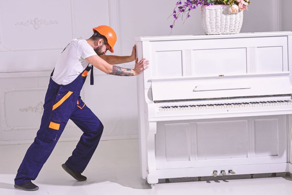 A Man is Pushing a White Piano in a Room — Bellarine Removals In Warrnambool, VIC