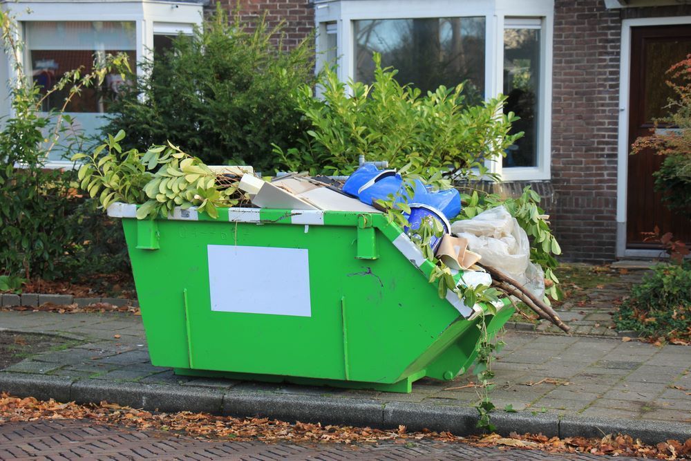 A Green Dumpster Filled With Garbage is on the Sidewalk in Front of a House — Bellarine Removals In Werribee, VIC