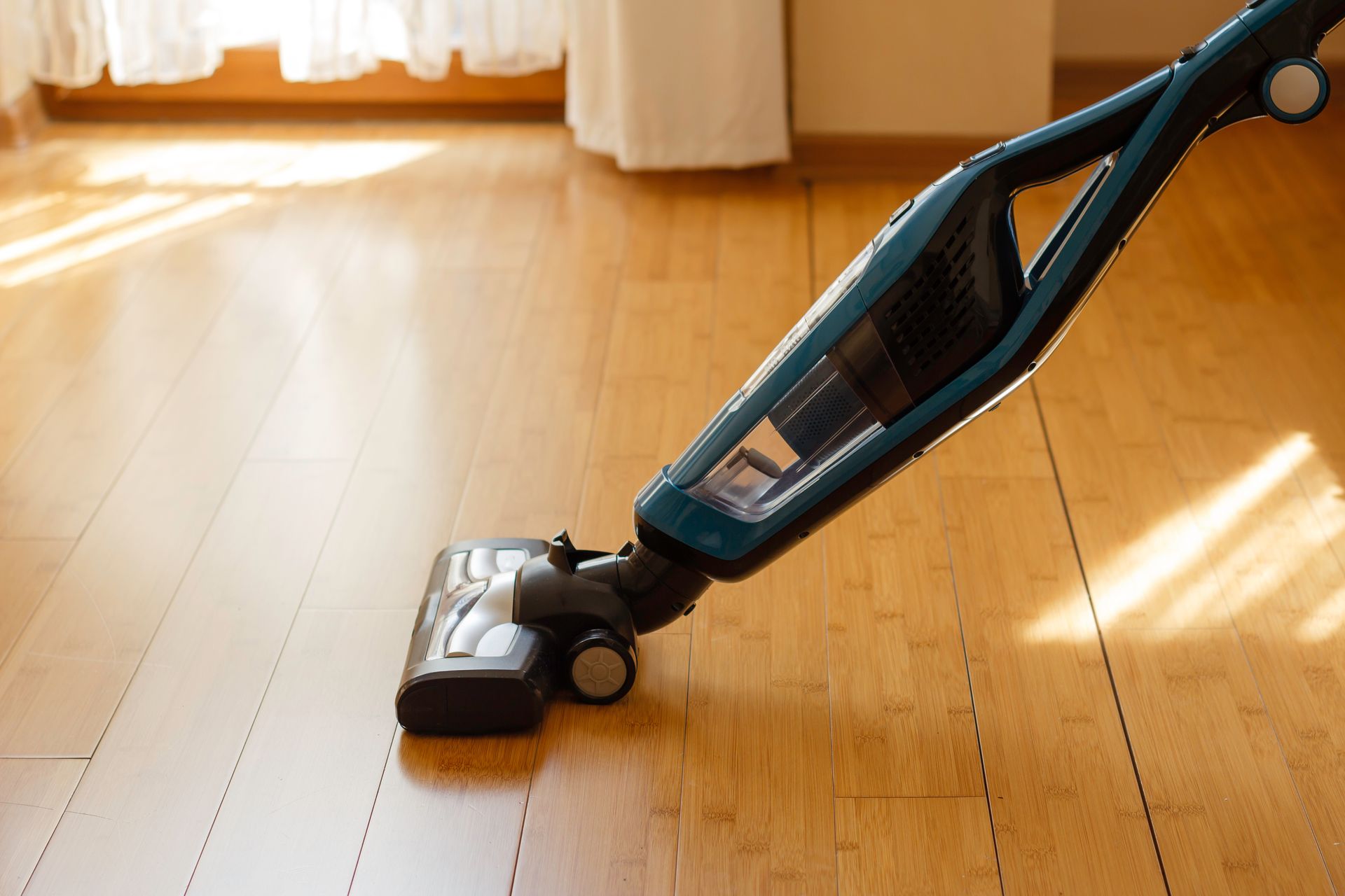 Cordless vacuum cleaning a sunlit wooden floor in a bright room.