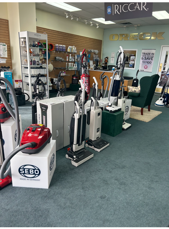 Vacuum cleaners on display in a store, with red, white, and silver appliances, and a green carpet.
