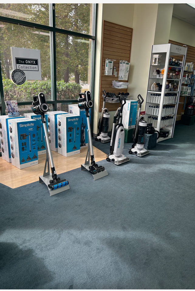 Vacuum cleaners displayed in a store, with boxes and shelving units visible.