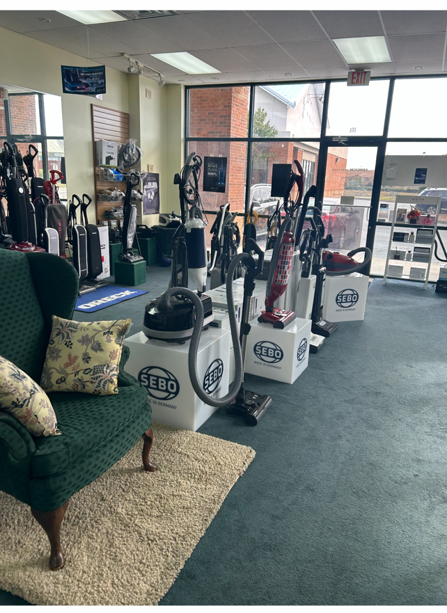 Vacuum cleaner store with various models on display, including a seating area with a green chair.