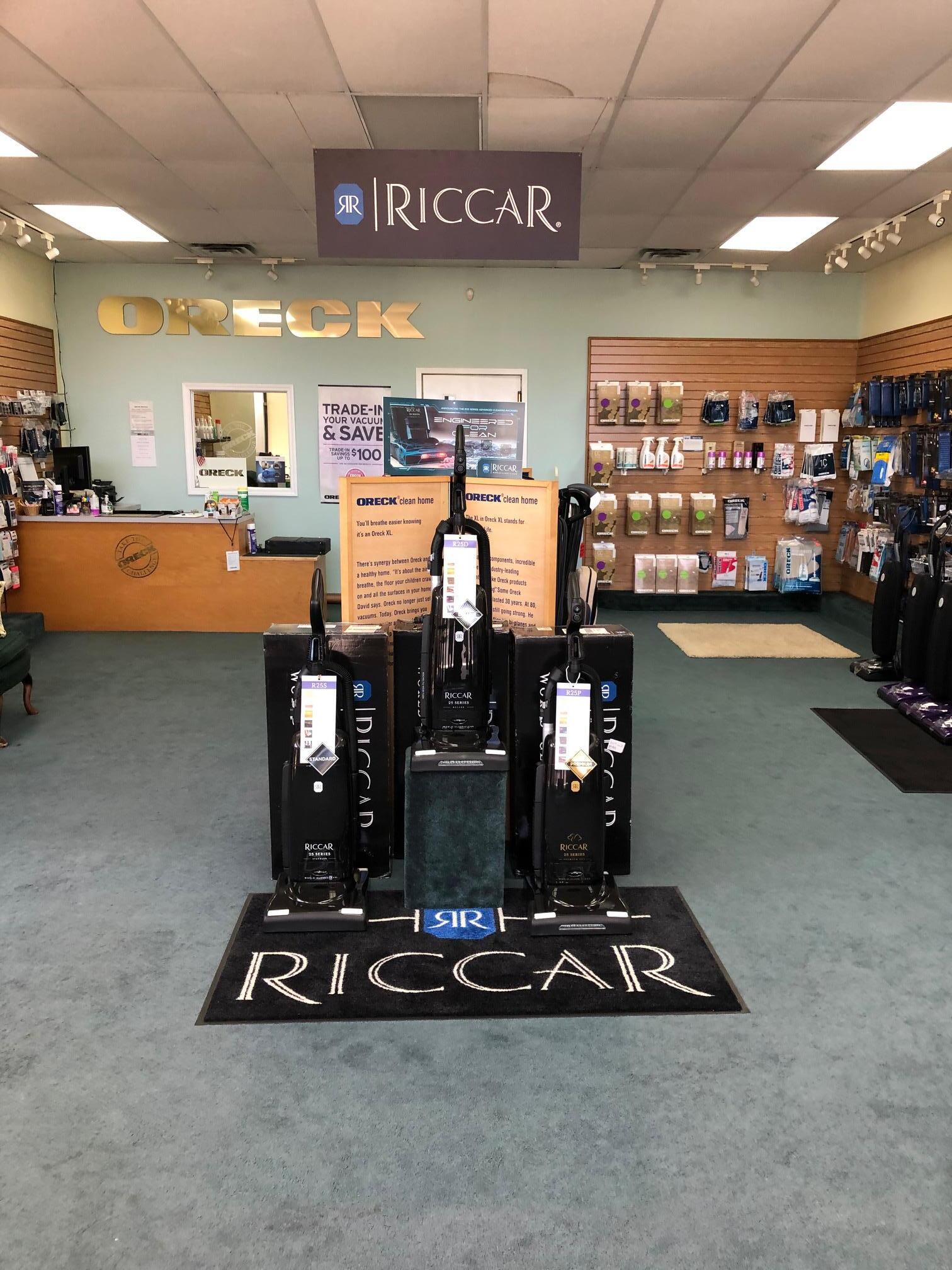 Vacuum display in a retail store, with Riccar signage overhead and a logo rug on the floor.
