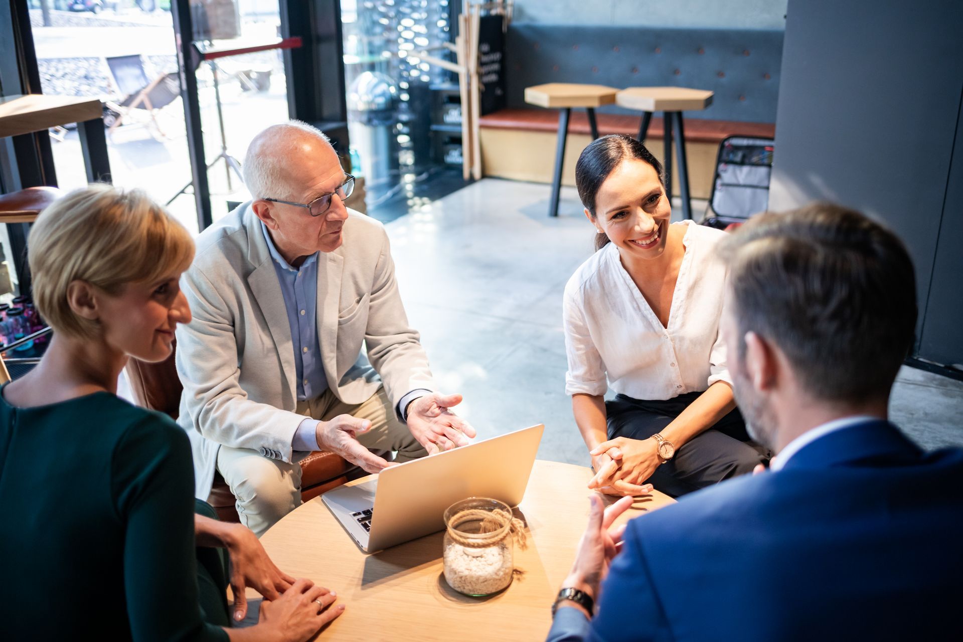 A group of people are sitting around a table with a laptop.