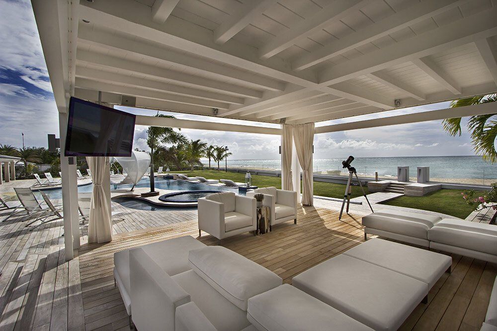 A living room with a couch , chairs , a television and a view of the ocean.
