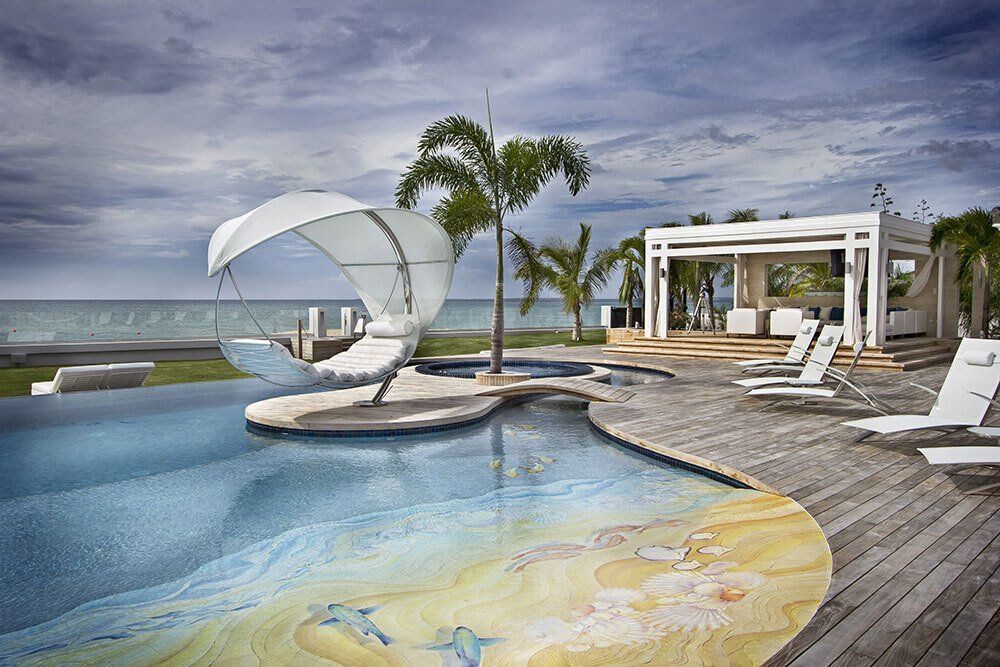 A large swimming pool surrounded by chairs and a gazebo overlooking the ocean.