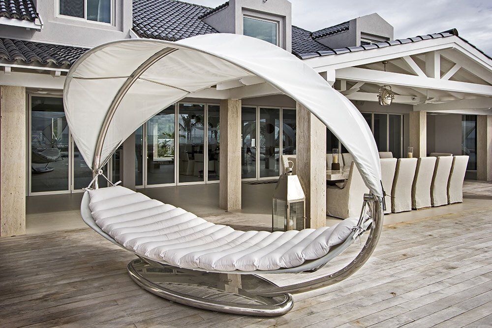 A white hammock is sitting on a wooden deck in front of a house