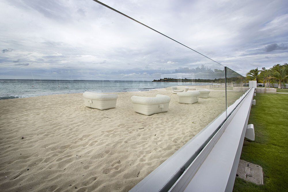 A glass fence surrounds a sandy beach with a view of the ocean.