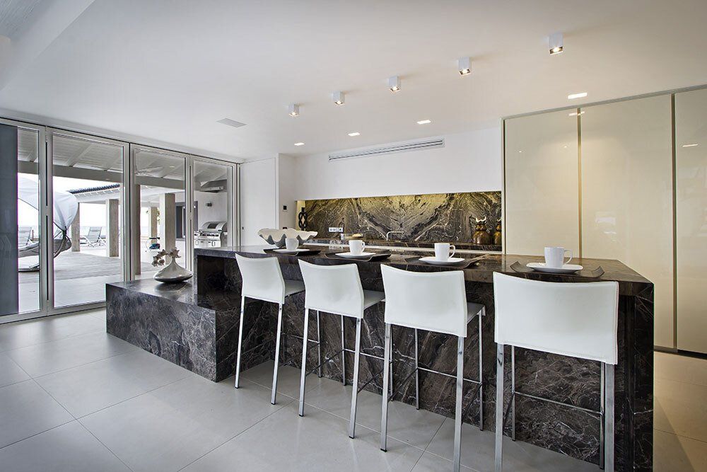 A kitchen with a marble counter top and white chairs