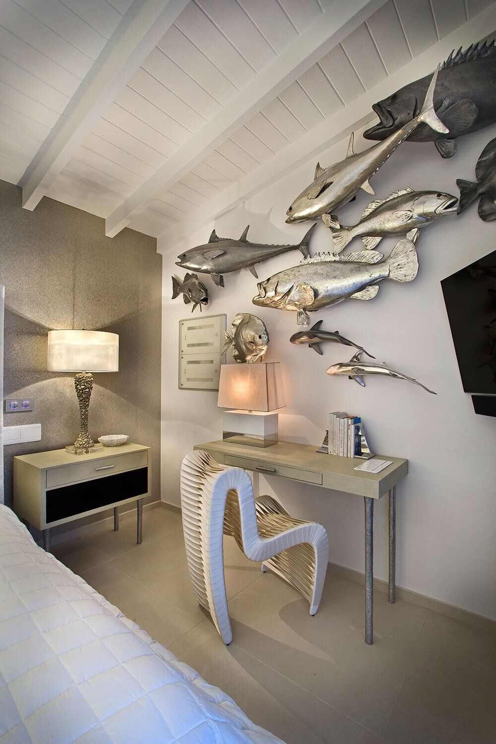 A bedroom with a desk , chair , lamp and fish on the wall.
