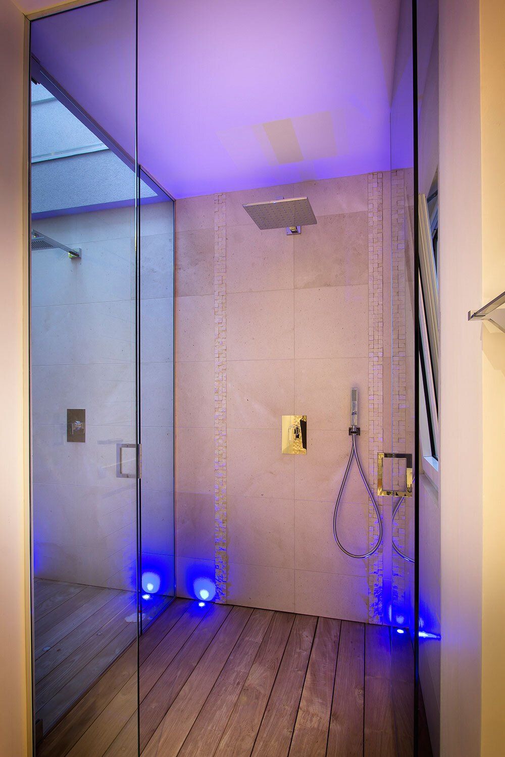 A bathroom with a walk in shower with a purple light on the ceiling.