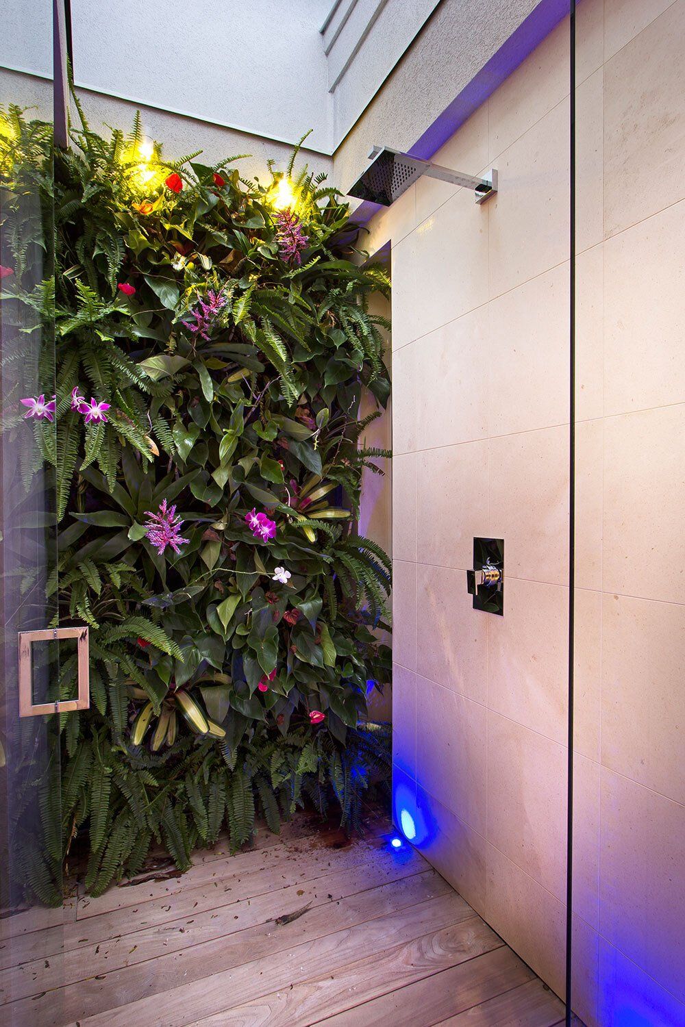 A shower with a wall of plants and flowers behind it.