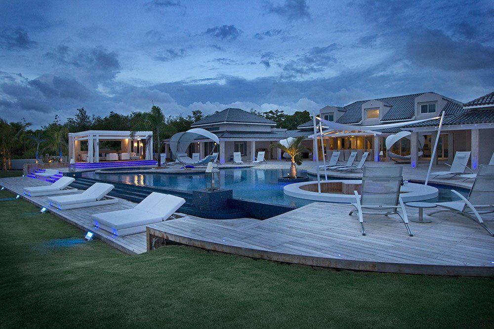 A large house with a swimming pool and chairs in front of it.