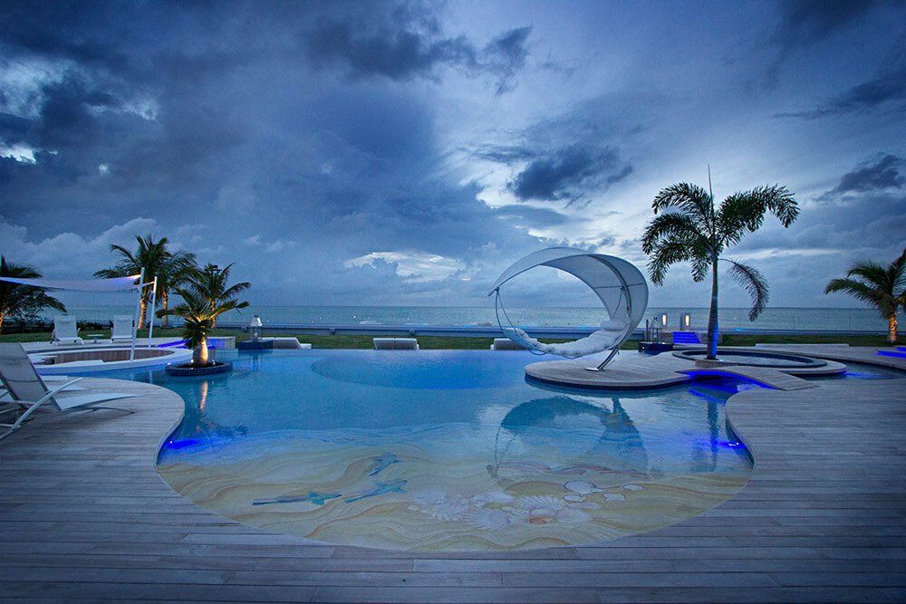 A large swimming pool surrounded by palm trees and a wooden deck overlooking the ocean.