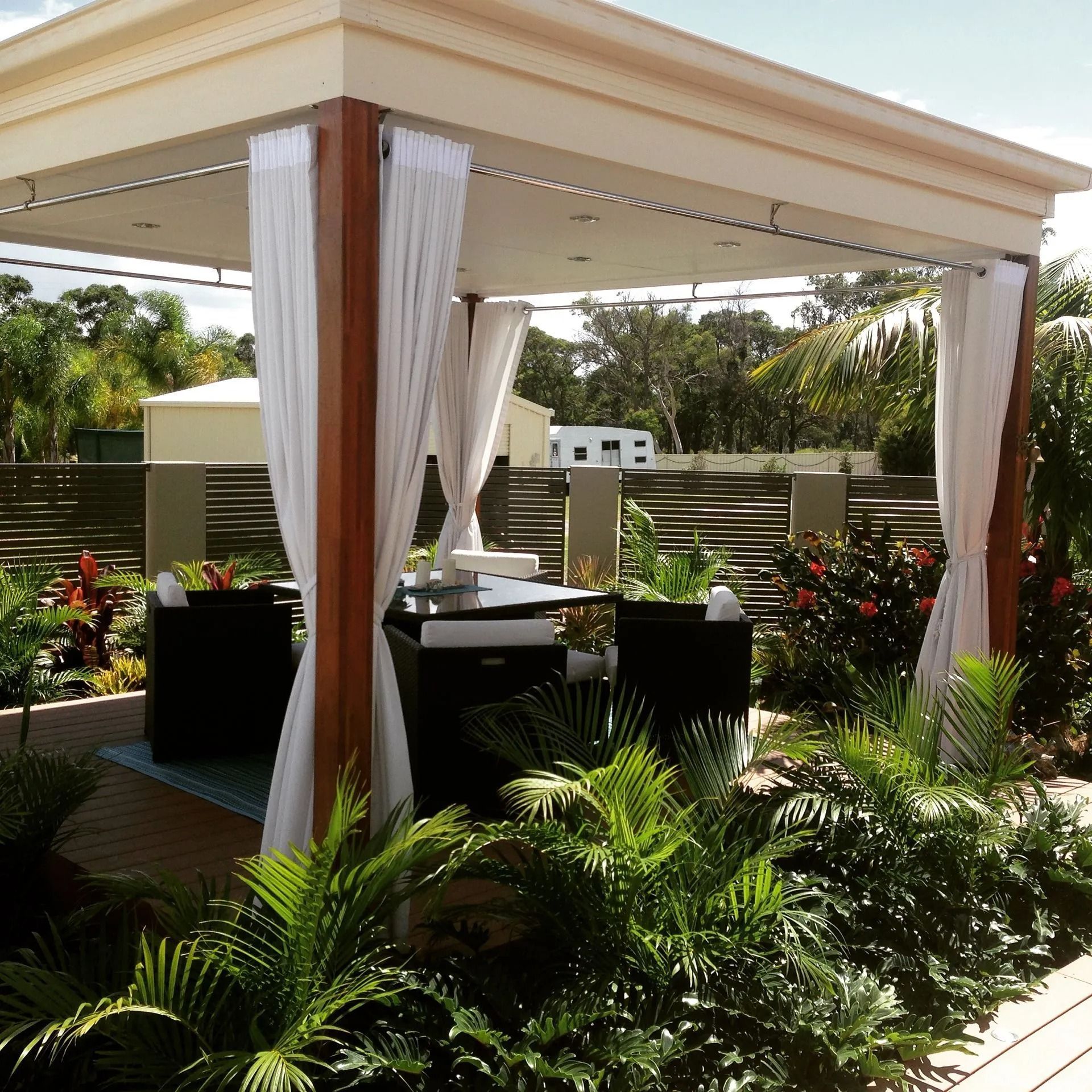 Gazebo With White Curtains, Dark Furniture, and Lush Tropical Plants — Divine Landscape Creations in Berkeley Vale, NSW