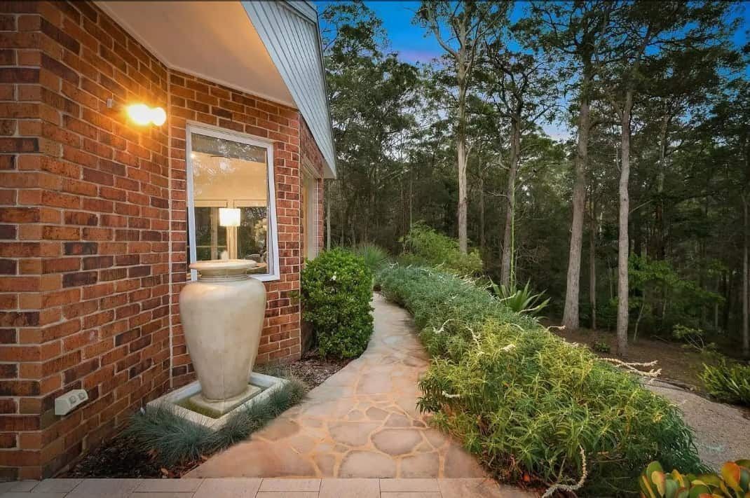 Brick Home Exterior With Stone Pathway Leading Through Landscaped Greenery — Divine Landscape Creations in Berkeley Vale, NSW