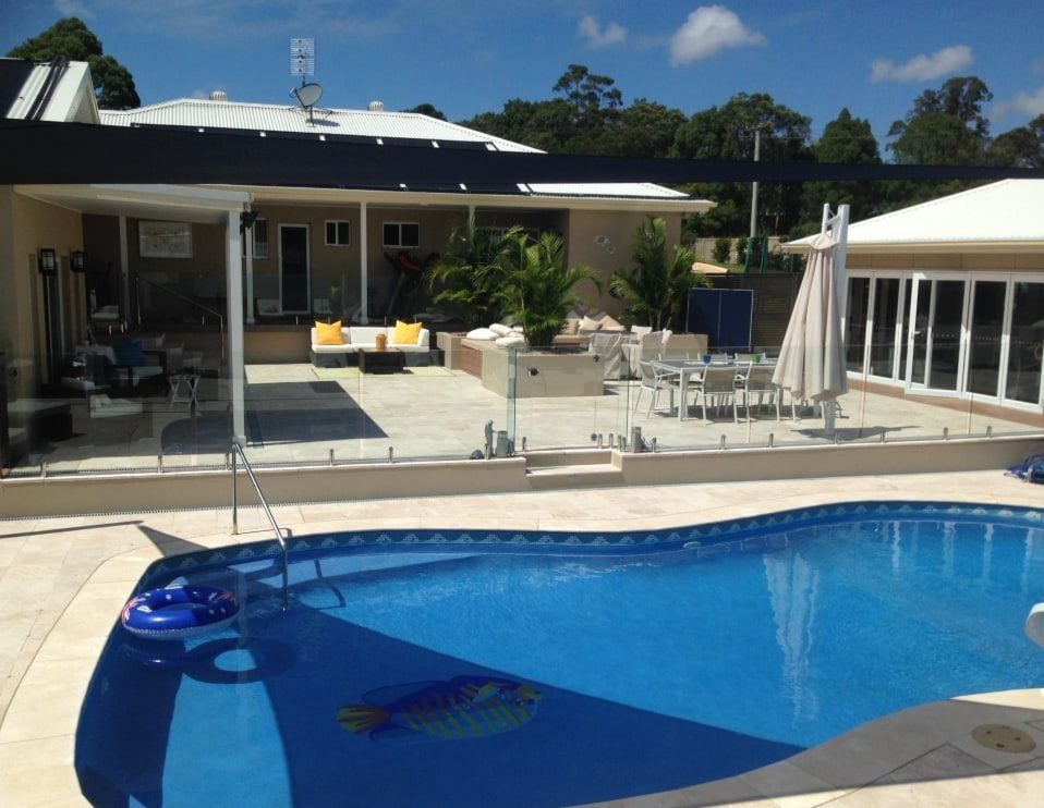 Swimming Pool With Outdoor Seating Area and Glass Fence on a Sunny Day — Divine Landscape Creations in Berkeley Vale, NSW