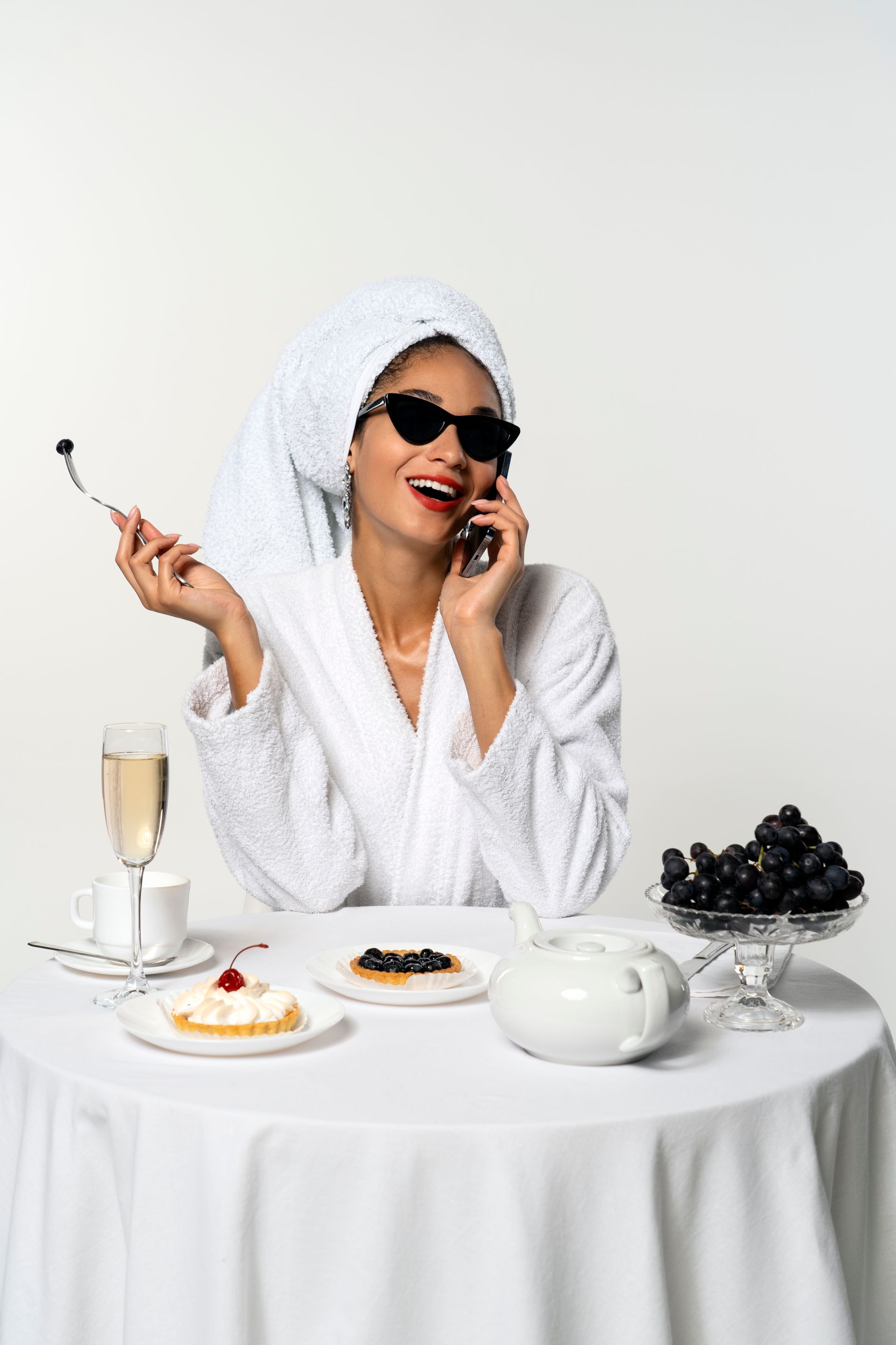 A woman in a bathrobe is sitting at a table talking on a cell phone.