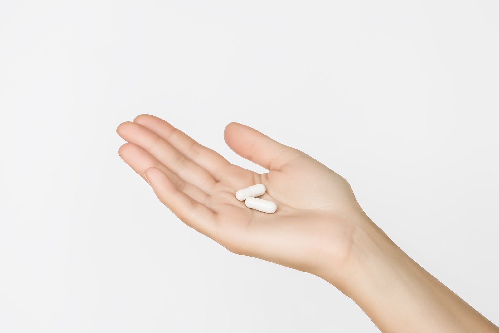 A woman 's hand is holding two white pills in her palm.