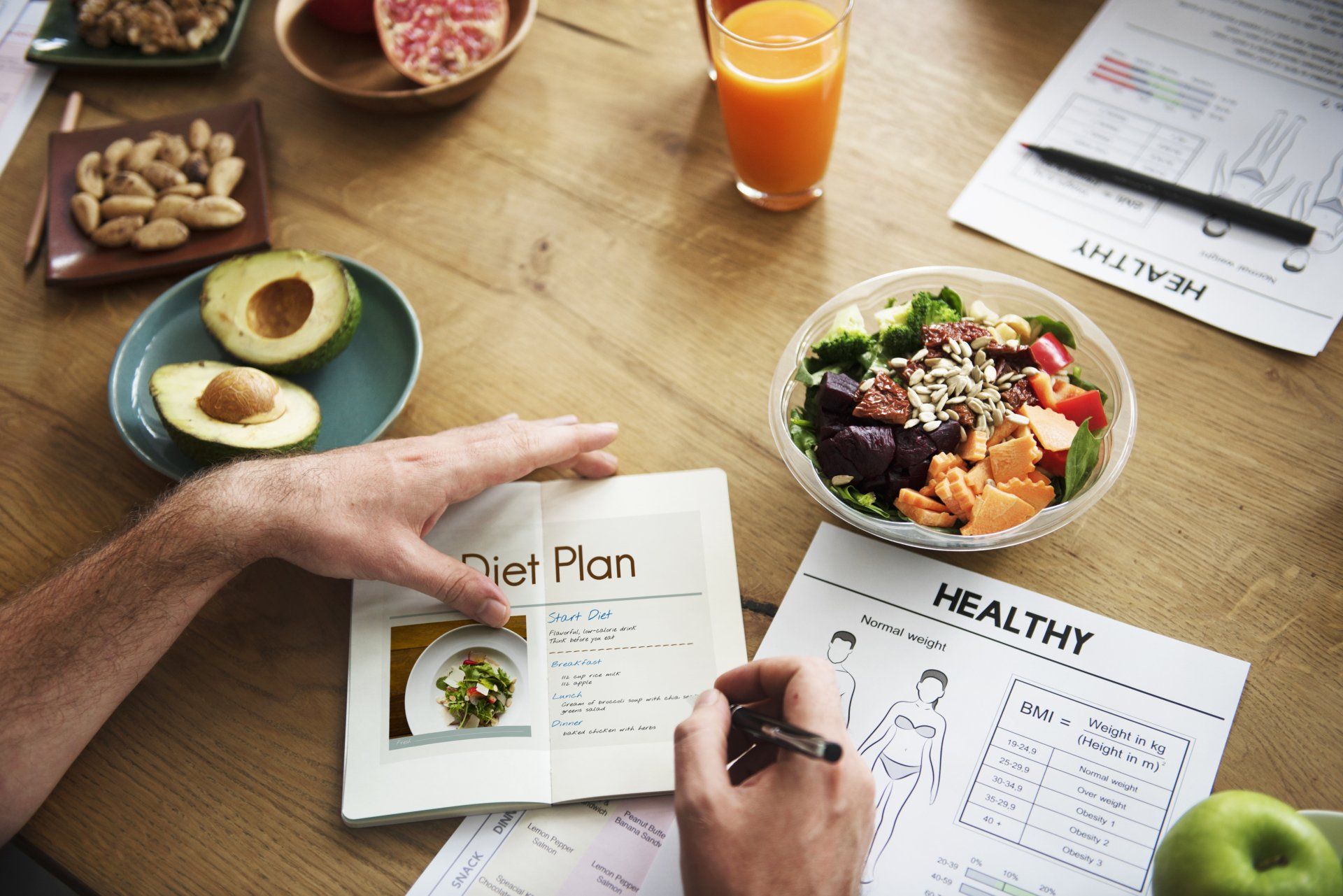 A man is writing in a notebook next to a bowl of salad.