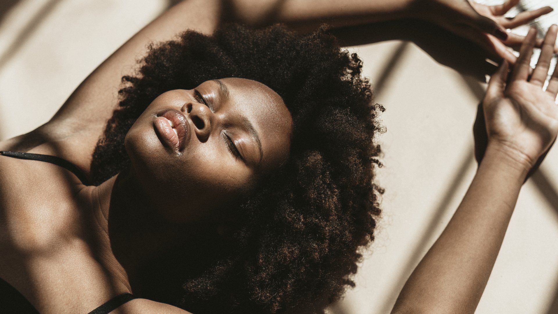 A woman is laying on her back with her eyes closed and her arms outstretched.