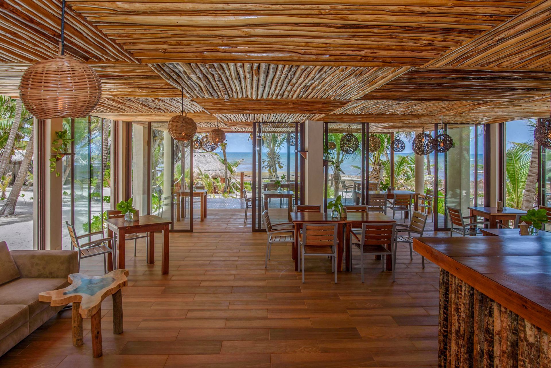 Interior of a beachside restaurant with wood ceiling, floors, tables, and open glass doors.