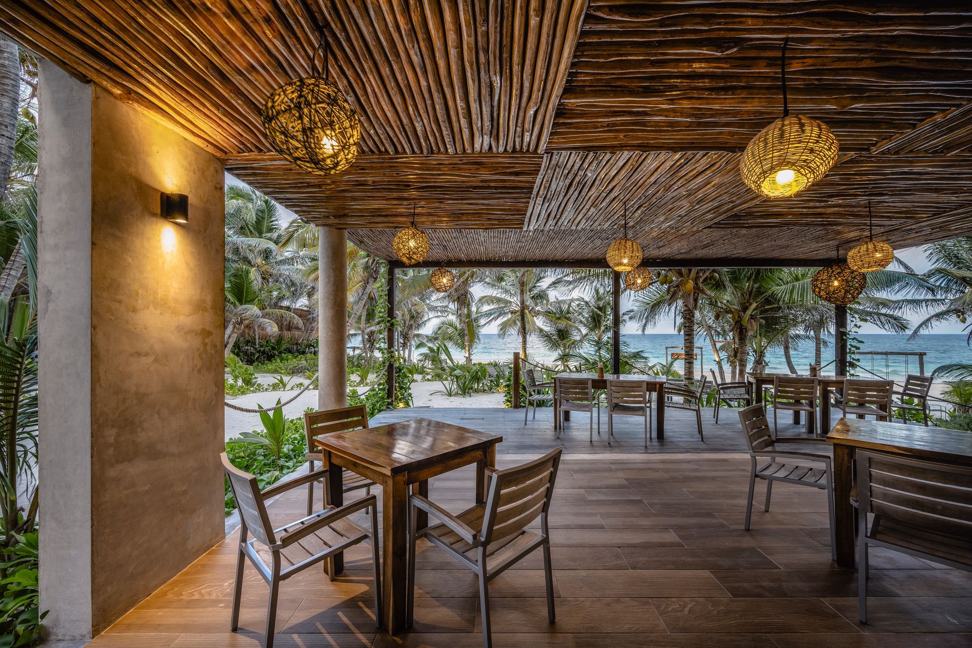 Beachside restaurant with wooden tables and chairs under a bamboo ceiling. Ocean view in the background.